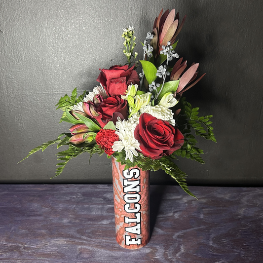 Bouquet of red and white flowers in a 'Falcons' themed vase on a dark surface with a gray background.