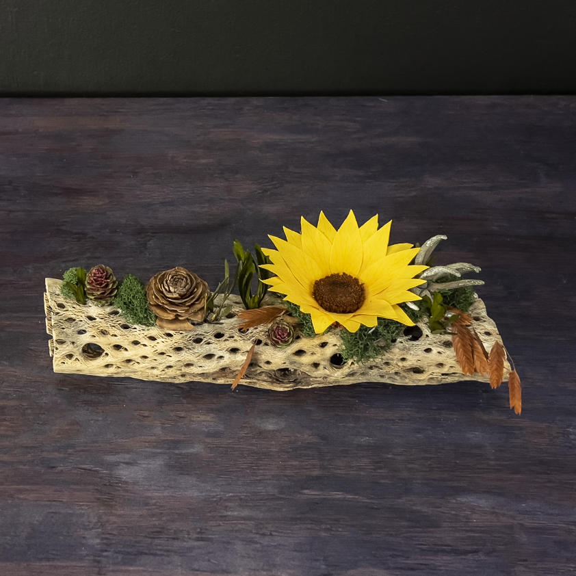 Decorative piece with a sunflower, pinecones, and leaves on a dark background