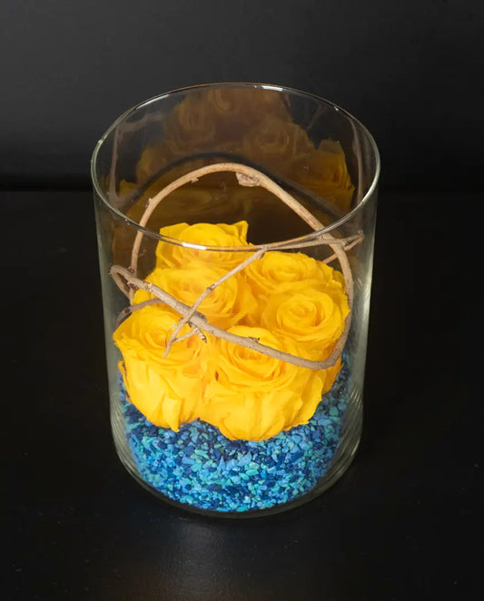 Glass vase with yellow roses and blue stones on a black background by bloombudz florist