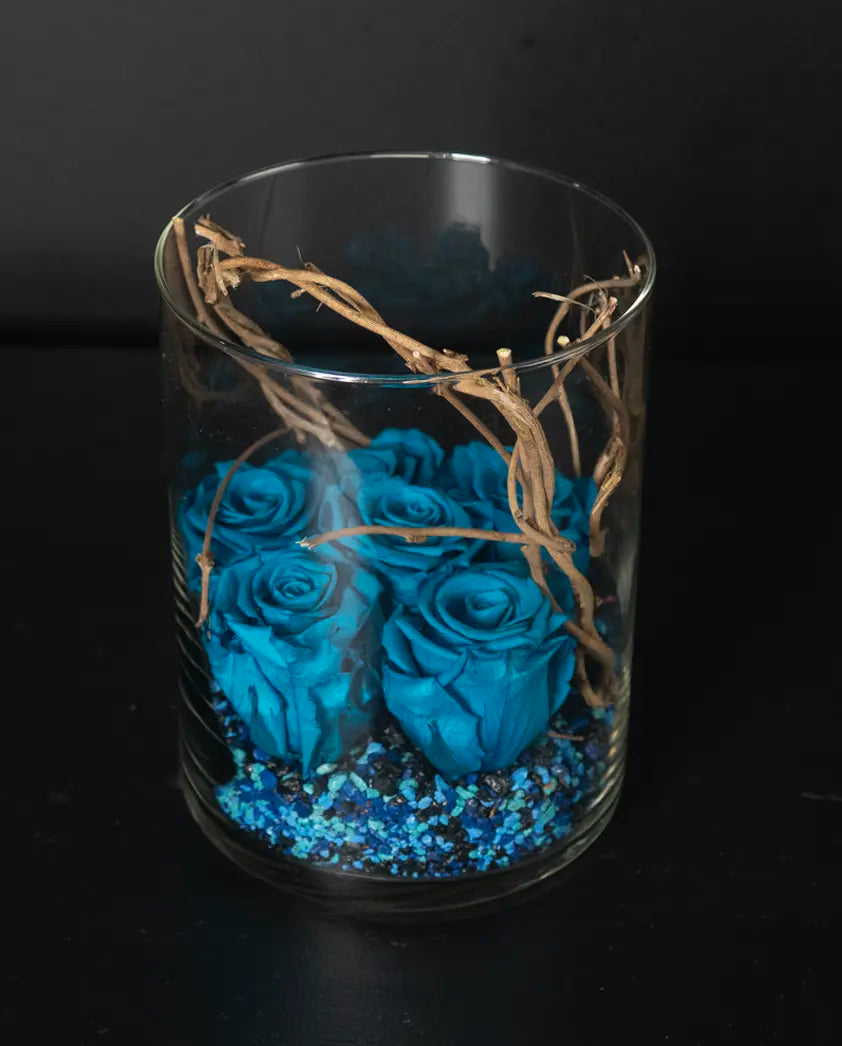 Glass vase with blue roses and decorative twine on a black background by bloombudz florist