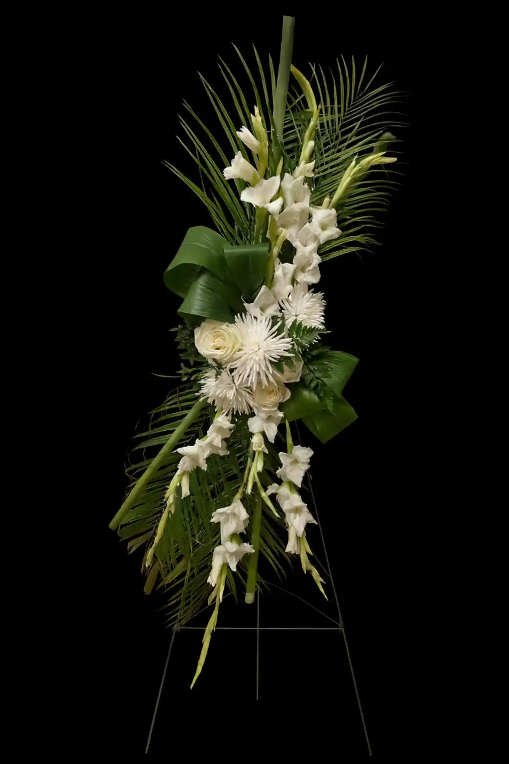 Standing spray floral arrangement with white flowers and green leaves on a black background