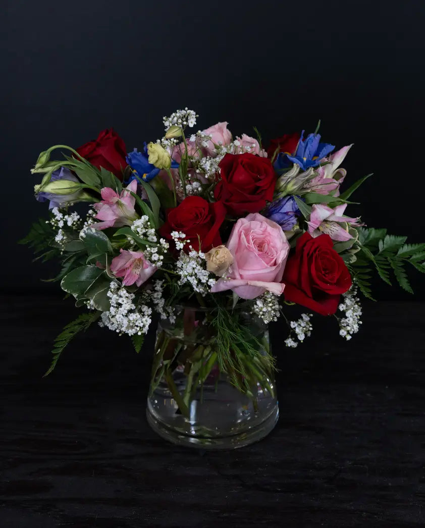 Bouquet of red, pink, and blue flowers in a clear vase on a black background