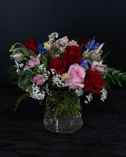 Bouquet of red, pink, and blue flowers in a clear vase on a black background