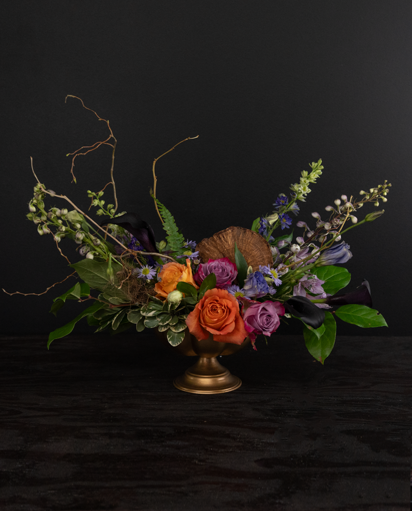 Floral arrangement with colorful flowers and greenery in a gold vase on a black background