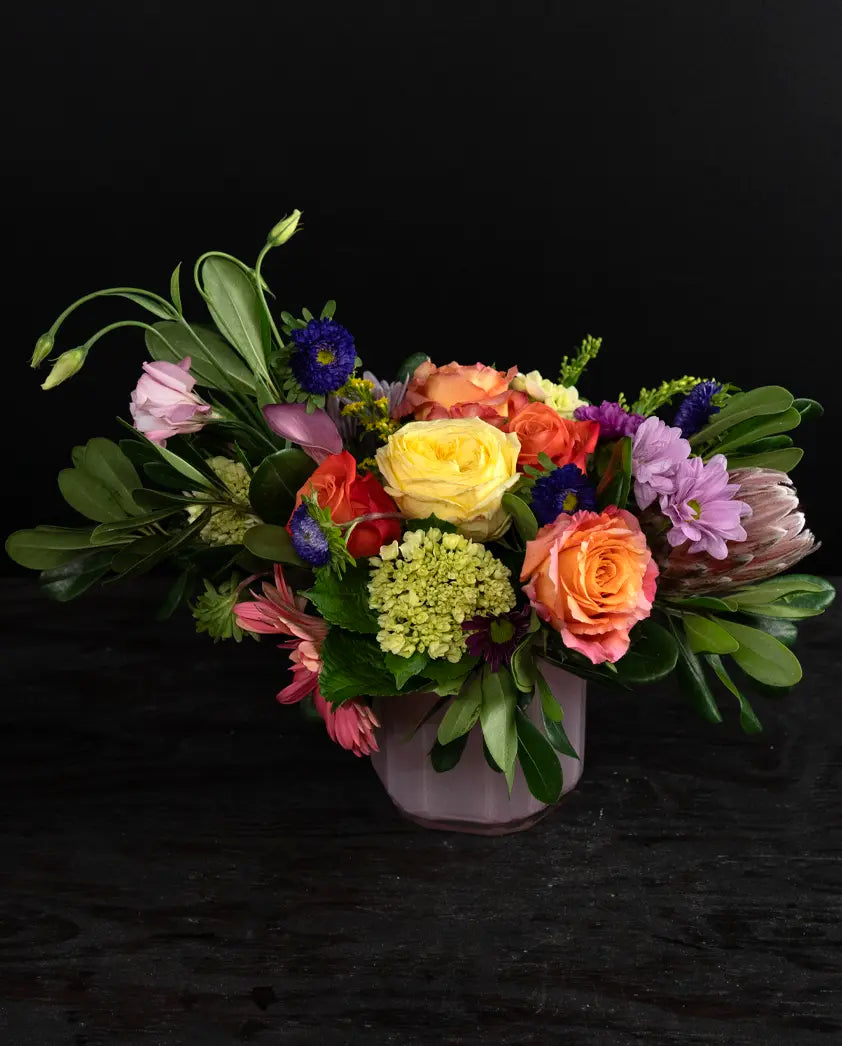 Colorful flower arrangement in a pink vase on a black background