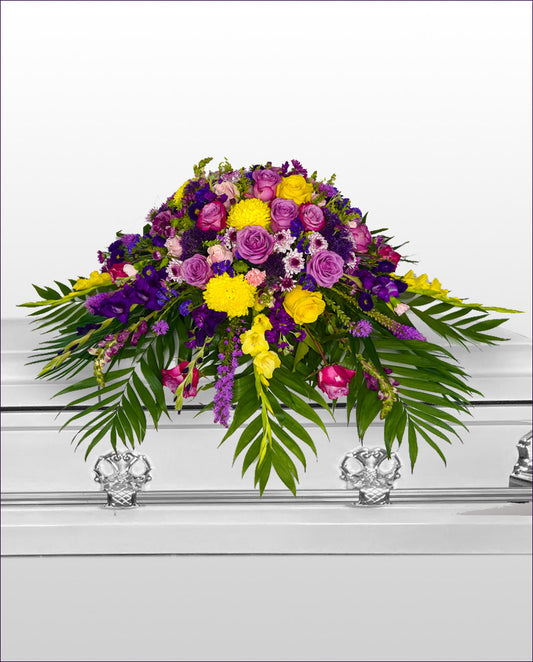 Colorful floral arrangement on a casket with purple, yellow, and green flowers.