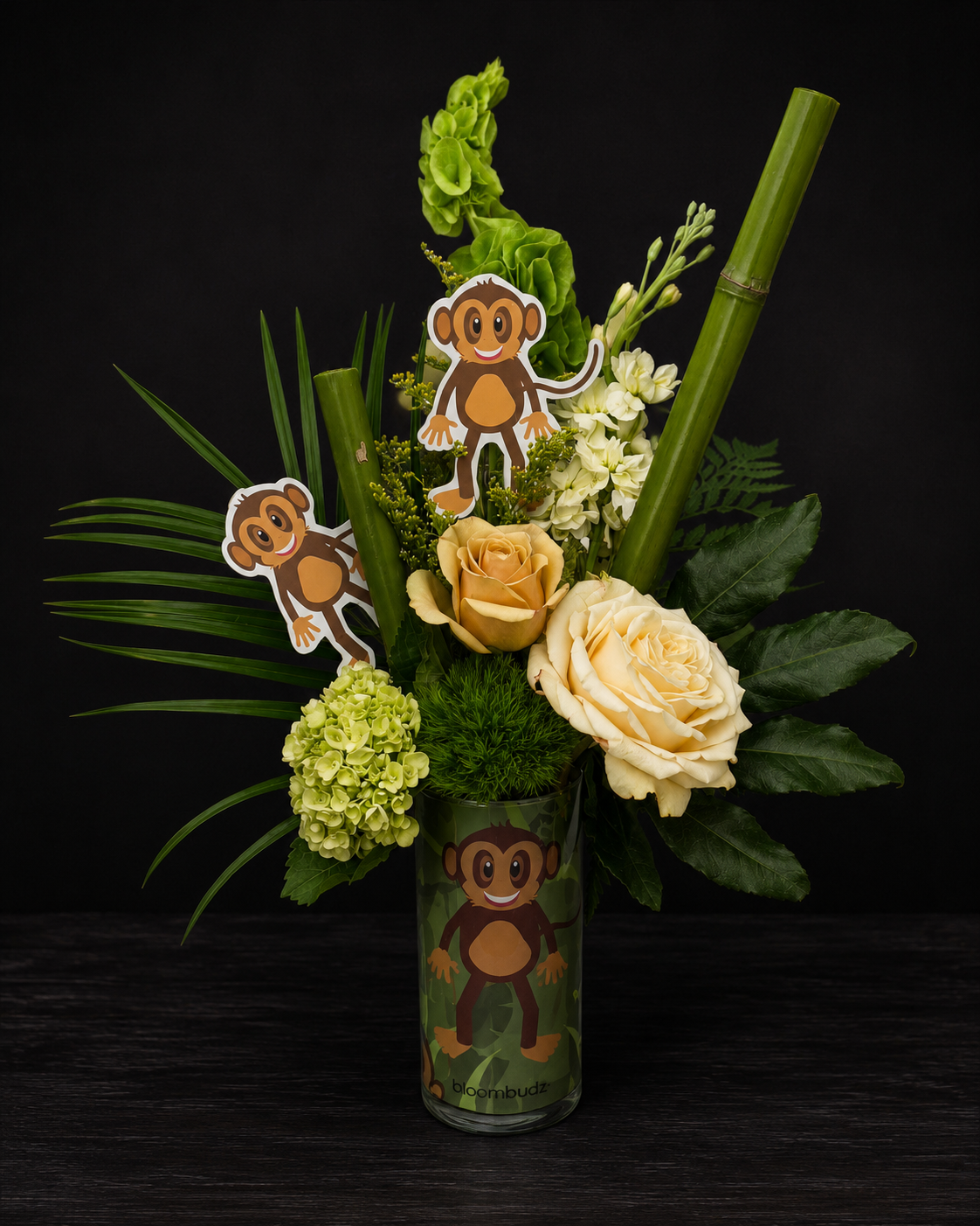 Floral arrangement with monkey-themed decorations in a clear vase on a dark background