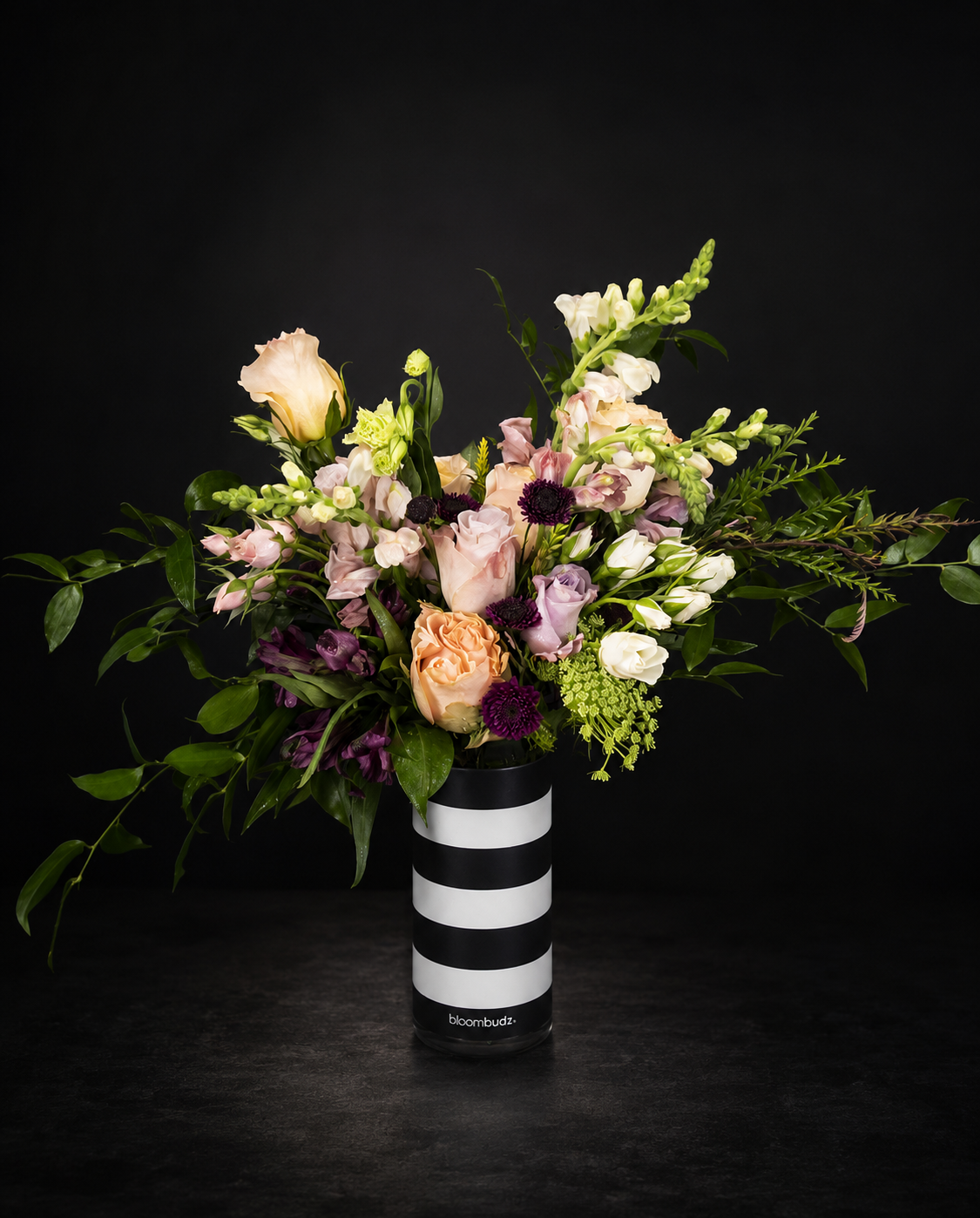 Bouquet of flowers in a black and white striped vase on a dark background