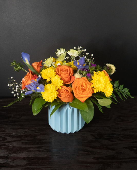 Colorful flower arrangement in a light blue vase on a dark surface